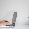 白い机でノートパソコンに向かって文章を打つ手元